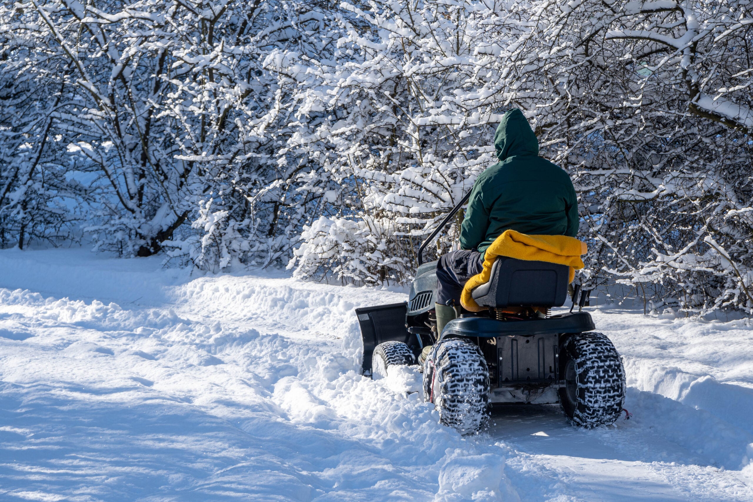 A rear view of a man riding snow blower clearing a snow-covered driveway
